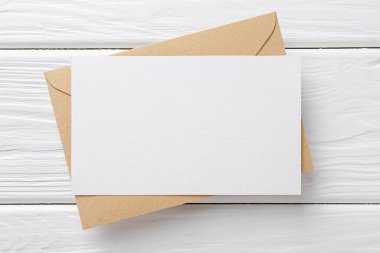 Beyaz ahşap masa üzerinde boş davetiye ve zarf, üst manzara. Tasarım için boşluk