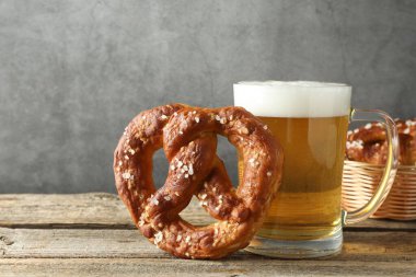 Lezzetli kraker ve bir bardak bira ahşap masada, gri arka planda, yakın planda.