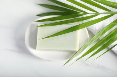 Beyaz mermer masanın üstünde sabun, havlu ve palmiye yaprağı var.