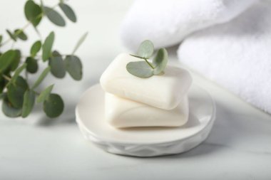 Sabun çubukları, havlular ve okaliptüs dalları beyaz mermer masa üzerinde, yakın plan.