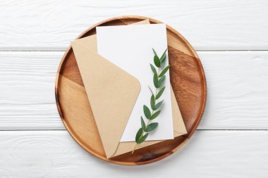 Boş davetiye kartı, zarf, tepsi ve dal beyaz ahşap masa, üst görünüm