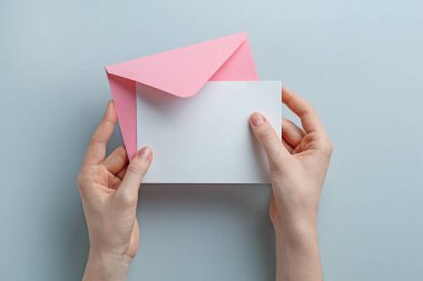 Gri arkaplanlı, üzerinde boş davetiye olan bir zarf tutan kadın. Tasarım için boşluk
