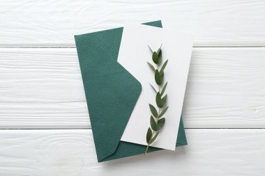 Boş davetiye kartı, zarf ve dal beyaz ahşap masa, üst görünüm