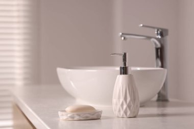 Banyodaki beyaz tezgahta sabun ve bir şişe kozmetik ürünü var.