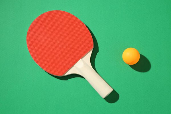 Ping pong racket and ball on green background, top view