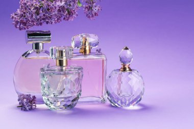 Parfümlü şişeler ve mor arkaplanda leylak çiçekleri, yakın plan.