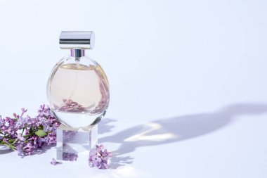 Parfüm şişesi ve açık gri arka planda leylak çiçekli dal, yakın plan. Metin için boşluk