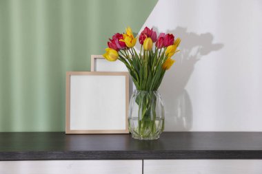 Renkli duvarın yanındaki masada bir buket güzel lale ve çerçeveler.