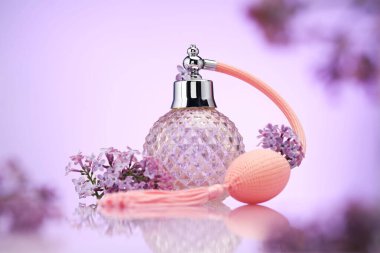 Bir şişe parfüm ve ayna yüzeyinde eflatun rengine karşı leylak çiçekleri, seçici odak
