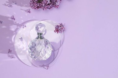 Bir şişe parfüm ve açık mor arka planda güzel leylak çiçekleri. Metin için boşluk