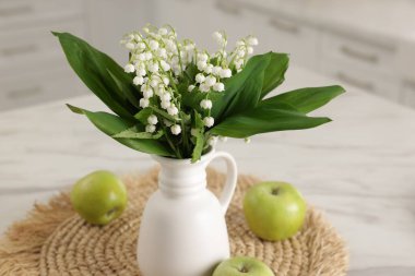 Vazodaki güzel zambak buketi ve mutfaktaki beyaz mermer masada elmalar.