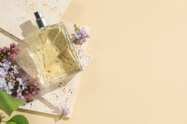 Bir şişe parfüm ve soluk sarı arka planda güzel leylak çiçekleri. Metin için boşluk