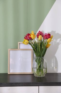 Renkli duvarın yanındaki masada bir buket güzel lale ve çerçeveler.
