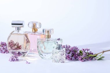 Açık gri arka planda leylak çiçekli parfüm şişeleri ve dallar, yakın plan.