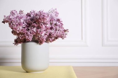 Beyaz duvarın yanındaki masada vazodaki güzel leylak çiçekleri, metin için yer var.