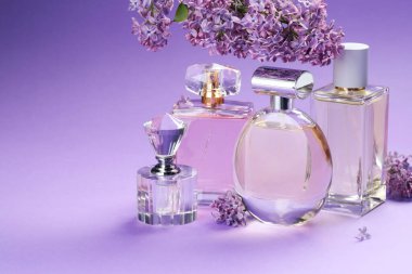 Parfümlü şişeler ve mor arkaplanda leylak çiçekleri, yakın plan. Metin için boşluk