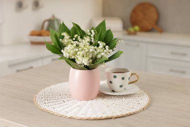 Vadideki güzel zambak buketi ve mutfaktaki ahşap masada duran kupa.