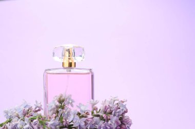 Parfüm şişesi ve mor arka planda leylak çiçekleri, yakın plan. Metin için boşluk