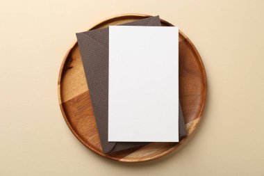 Boş davetiye kartı, zarf ve bej arka planda ahşap tepsi, üst görünüm