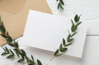 Boş davetiye kartı, zarf ve dallar beyaz ahşap masada, düz yerde. Tasarım için boşluk