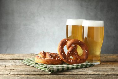 Lezzetli krakerler ve bira bardakları ahşap masada gri arka planda, yakın plan