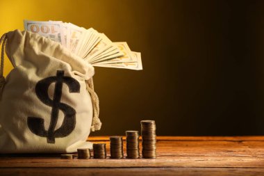 Dolar banknotları ve ahşap masaya istiflenmiş bozuk paralarla dolu çanta, sarı eğimli arkaplan, metin için boşluk