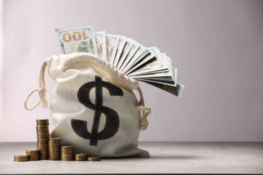Dolar banknotları ve gri masanın üzerine yığılmış bozuk paralarla dolu bir çanta. Işık arkaplanı, metin için boşluk.