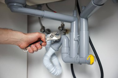 Tesisatçı, lavabonun altındaki boruları tamir ediyor. Kapalı.