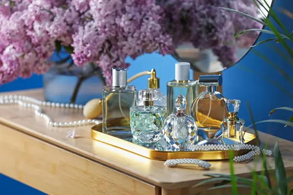 Parfümlü şişeler, eflatun çiçekleri ve tuvalet masasında aksesuarlar.