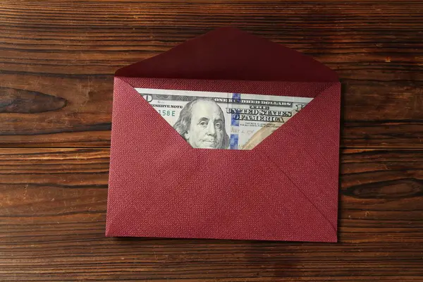 Para bonusu. Tahta masanın üstünde dolar banknotuyla zarf, üst manzara.