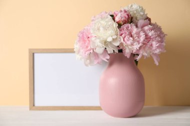 Vazodaki güzel şakayıklar ve bej arka plandaki beyaz masa üzerindeki resim çerçevesi