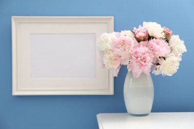 Vazodaki güzel şakayıklar ve resim çerçevesi açık mavi duvarın yanındaki beyaz masada.