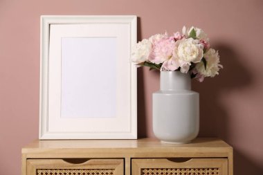 Vazodaki güzel şakayıklar ve pembe duvarın yanındaki ahşap şifoniyerin üzerindeki resim çerçevesi. Metin için boşluk