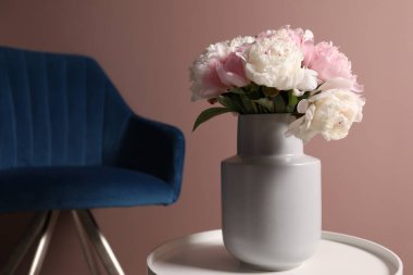 Beyaz masadaki vazodaki güzel şakayıklar ve pembe duvarın yanındaki koltuk.