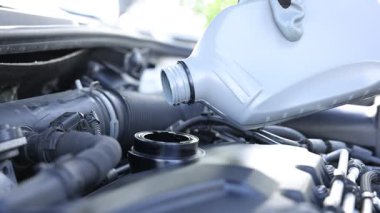 İşçi motor yağını teneke kutudan araba motoruna boşaltıyor.