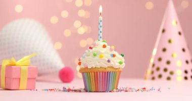 Kekin üzerine mum üfleme, yakın plan. Pembe arka planda bulanık ışıklarla parti dekoru