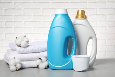 Beyaz tuğla duvara karşı gri masada yumuşatıcı, havlu ve pamuk çiçekleri.