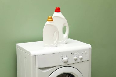 Çamaşır makinesinin üzerinde soluk yeşil duvarın yanında yumuşatıcı şişeler.