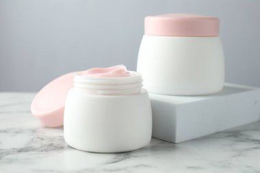 Kavanozlar dolusu nemlendirici vücut kremi beyaz mermer masada, yakın plan.