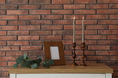 Mum ve tuğla duvarın yanındaki masada yanan mumlar.