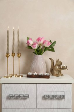Mumları yanan zarif şamdanlar vazoda laleler ve bej duvarın yanındaki şifoniyerde diğer dekorlar.