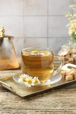 Cam bardakta nefis papatya çayı, taze çiçekler, kahverengi şeker ve çaydanlık ahşap masada, yakın plan.