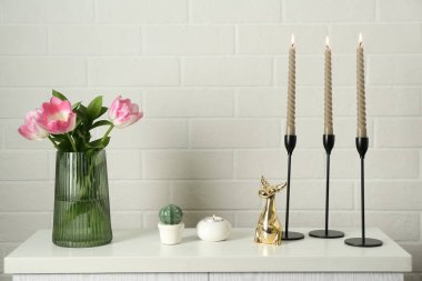 Yanan mumları olan zarif şamdanlar vazoda laleler ve beyaz tuğla duvarın yanındaki şifoniyerde diğer dekorlar.