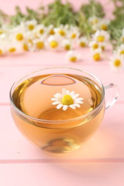 Cam bardakta nefis papatya çayı ve pembe ahşap masada taze çiçekler, yakın plan.