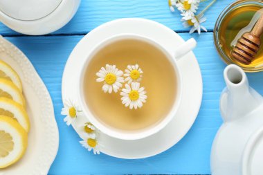 Lezzetli papatya çayı, taze çiçekler, limon ve bal açık mavi ahşap masa, düz uzanmış