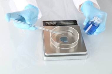 Laboratuvardaki beyaz ayna masasında numune ve terazilerle çalışan bilim adamı.