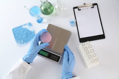 Beyaz masada Petri kabı ve ölçekleriyle çalışan bilim adamı.