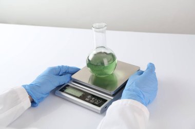 Bilim adamı beyaz masadaki terazide numune tartıyor, yakın plan.