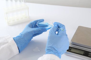 Bilim adamı, beyaz masadaki terazilerin yakınında numuneyle çalışıyor.