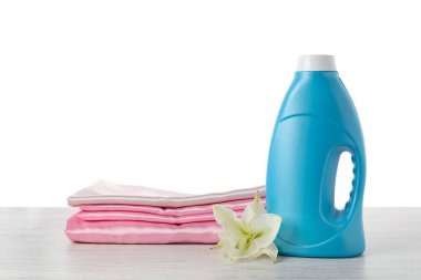 Bir şişe yumuşatıcı, üst üste yığılmış giysiler ve çiçek beyaz arka plana karşı ahşap masa